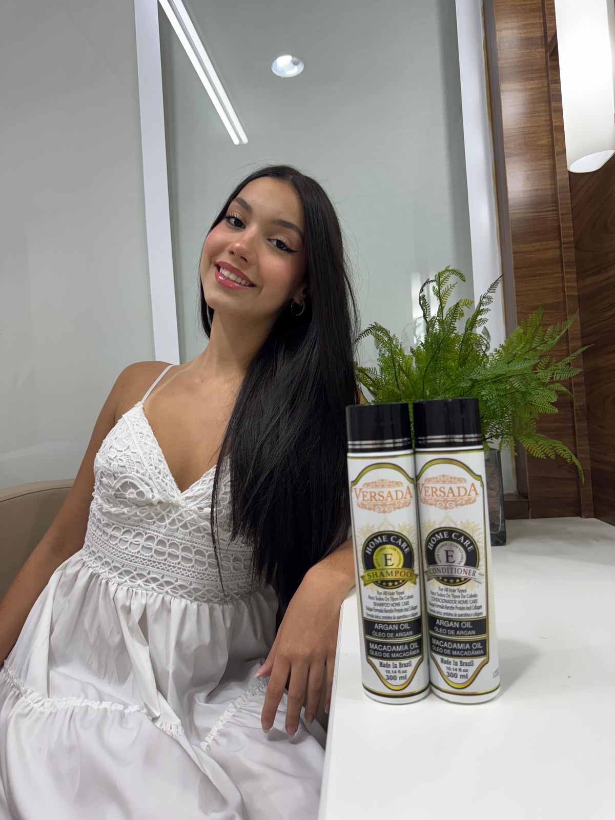 Woman in a white dress sitting next to two bottles of Versada hair care products.